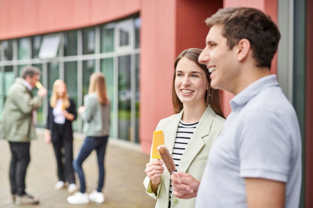 Mitarbeitende stehen draußen und unterhalten sich, während sie ein Eis essen