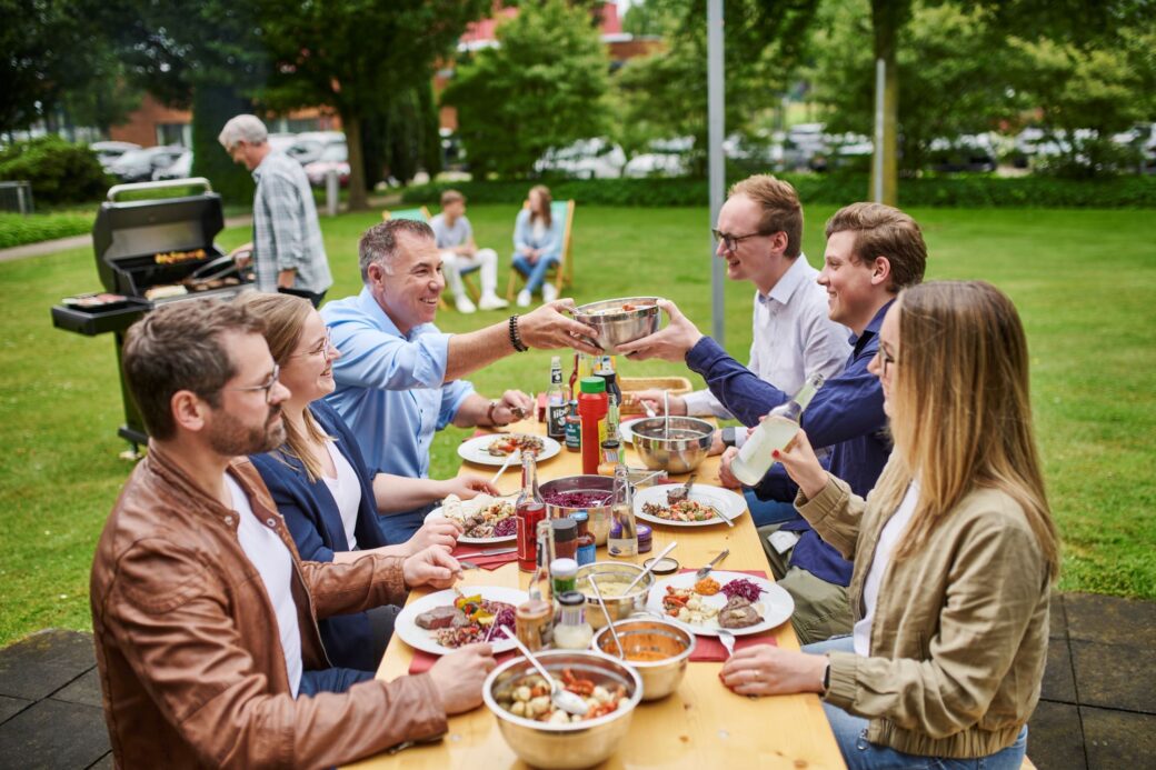 Mitarbeitende sitzen gemeinsam an einem Tisch und essen Gerichte vom Grill
