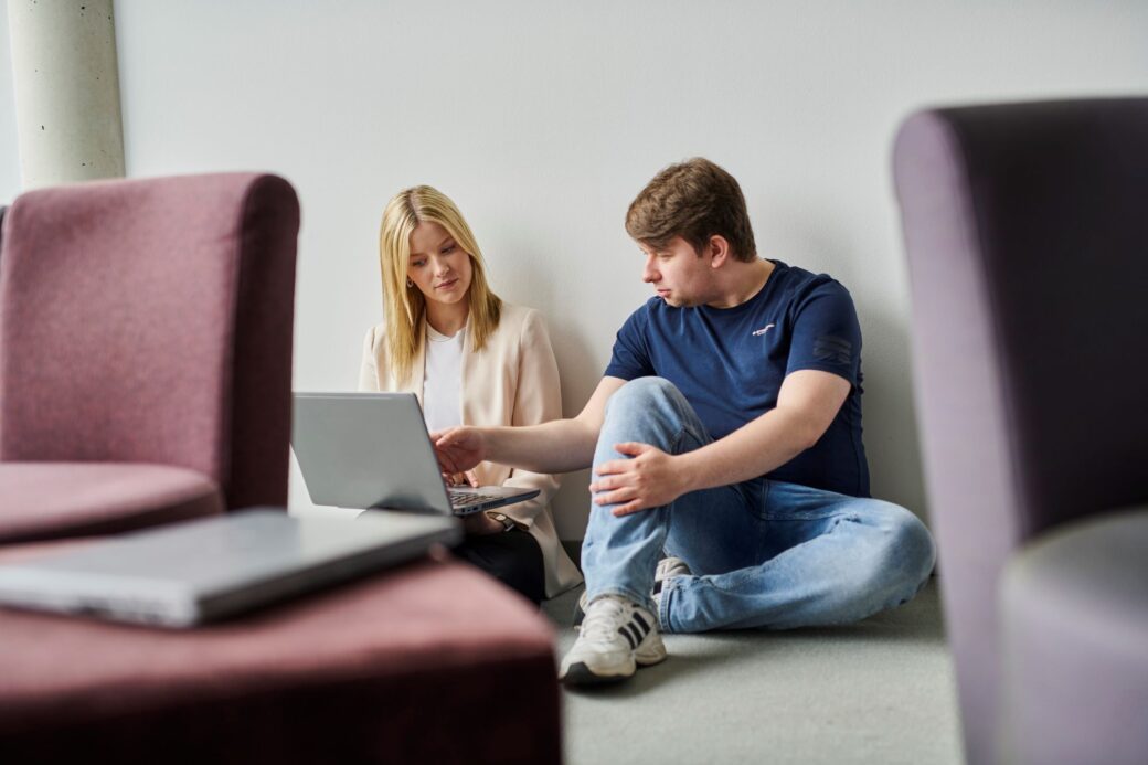 Mitarbeitende sitzten zusammen auf dem Boden und schauen gemeinsam auf einen Laptop
