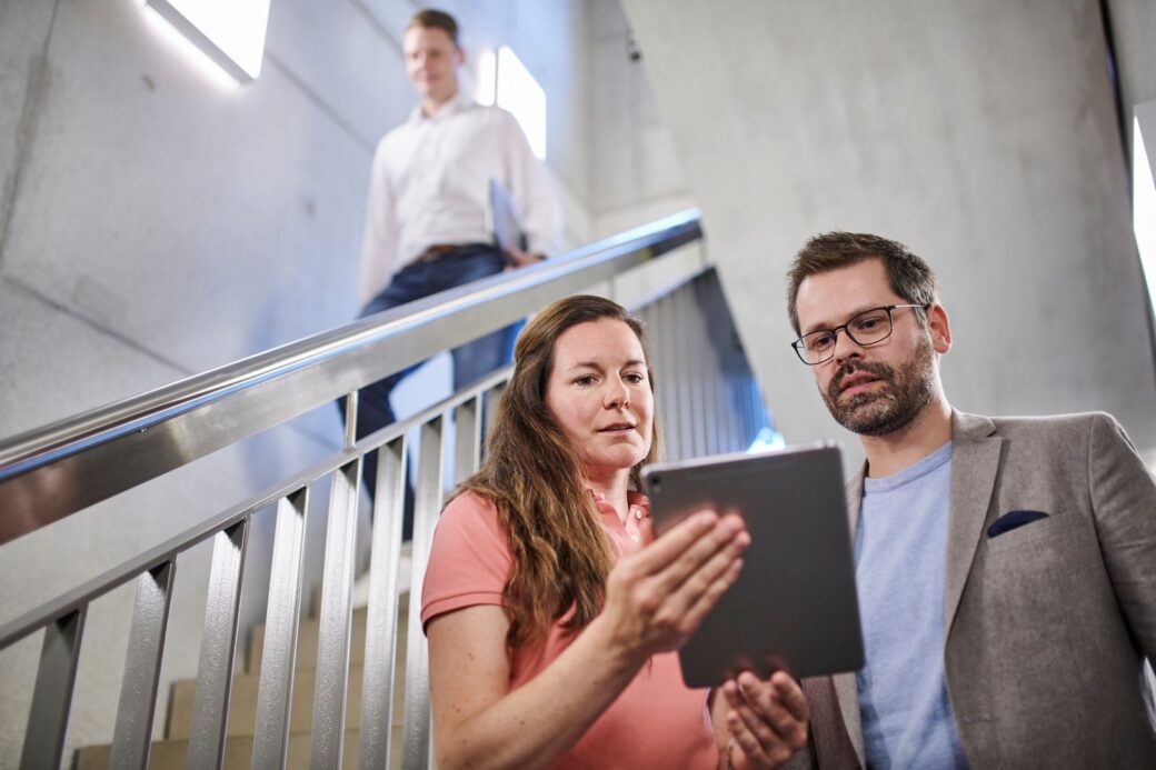 Mitarbeitende stehen im Treppenhaus und schauen gemeinsam auf eine Tablet