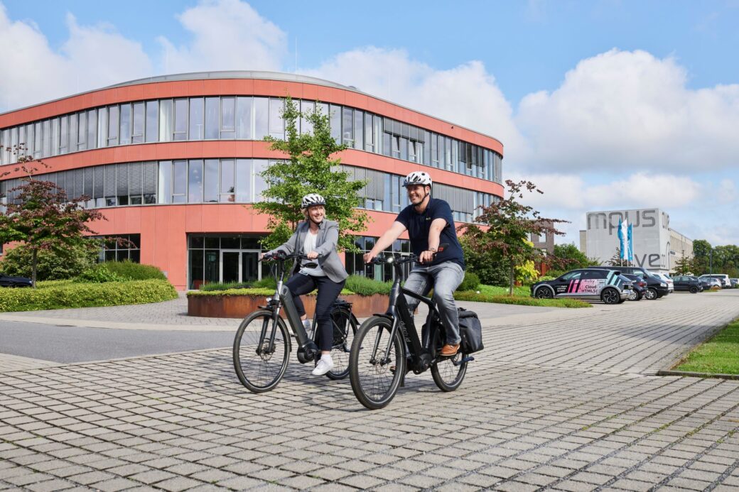 Zwei Mitarbeiter fahren auf ihren Fahrrädern vom Campus-Gelände