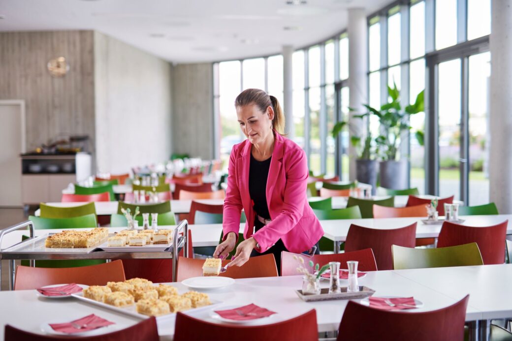 Mitarbeiterin deckt die Tische in der Kantine mit Geschirr und Kuchen ein